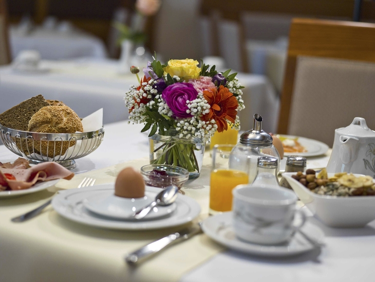 Frühstückstisch mit Brötchen, Blumenstrauß und Saft in einem Hotelrestaurant.