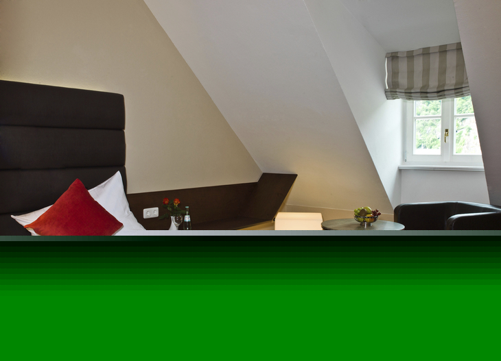 Einzelzimmer mit Bett, Sessel und Tisch in einem Hotel unter Dachschräge.