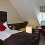 Einzelzimmer mit Bett, Sessel und Tisch in einem Hotel unter Dachschräge.