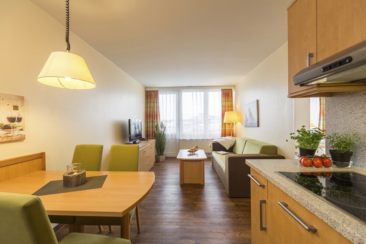 Wohnzimmer mit Esstisch, Sofa, Fernseher, Hängelampe und Küchenbereich.