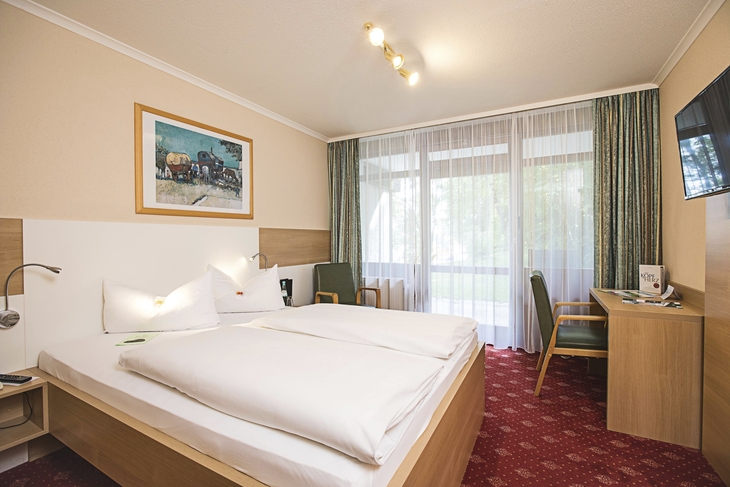 Doppelzimmer mit Doppelbett, Schreibtisch und Balkon im Hotel.