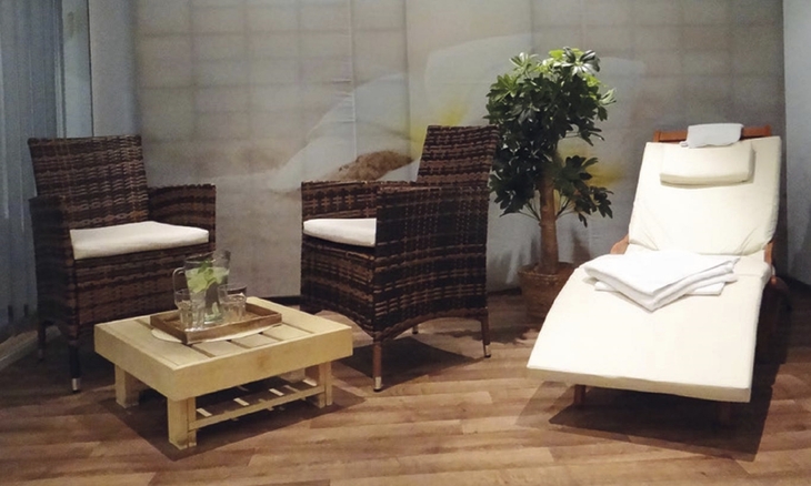 Zwei Korbsessel, ein Tisch mit Wasserkrug und ein Liegestuhl in einem Wellnessraum.