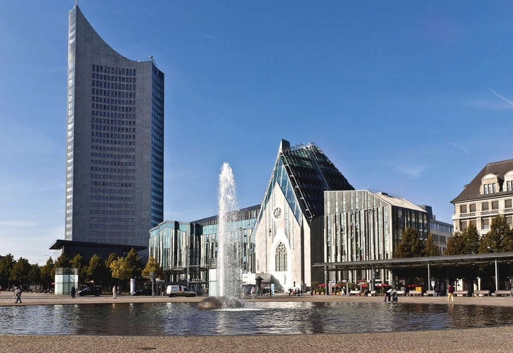 Neues Augusteum Leipzig mit Wasserfontäne im Vordergrund bei klarem Himmel.