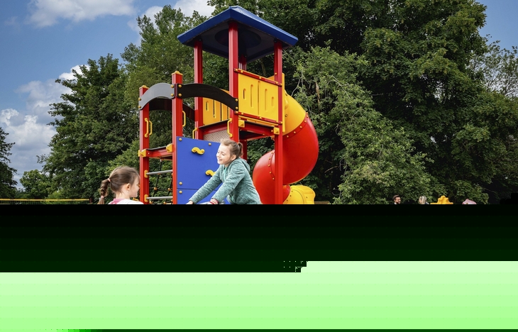 Zwei Kinder spielen auf einem Spielplatz mit Rutsche und Federwippe im Freien.