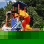 Zwei Kinder spielen auf einem Spielplatz mit Rutsche und Federwippe im Freien.