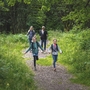 Familie wandert im Wald, zwei Kinder rennen auf einem Pfad voraus.
