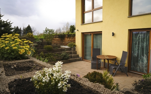Rückansicht eines Hauses mit Terrasse, Pflanzen und Gartenmöbeln.