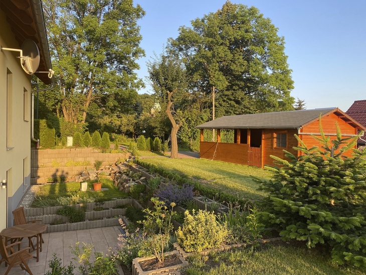 Garten mit Holzhaus, Bäumen und Terrasse bei Sonnenuntergang.