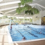 Menschen schwimmen in einem Hallenbad mit Rutsche und großen Fenstern.