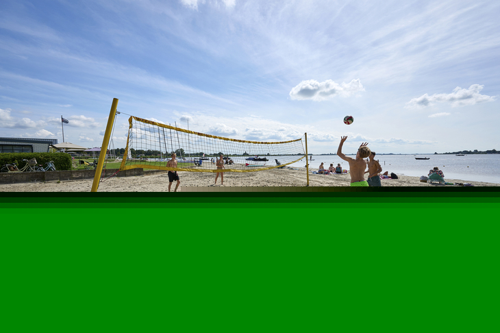 Personen spielen Beachvolleyball am Sandstrand bei sonnigem Wetter.