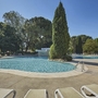 Poolbereich mit Liegestühlen und umliegenden Bäumen an einem sonnigen Tag.