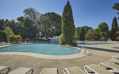 Poolbereich mit Liegestühlen und umliegenden Bäumen an einem sonnigen Tag.