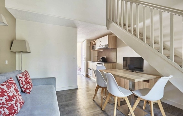 Wohnbereich mit Sofa, Tisch, Stühlen und Küchenzeile, Treppe im Hintergrund