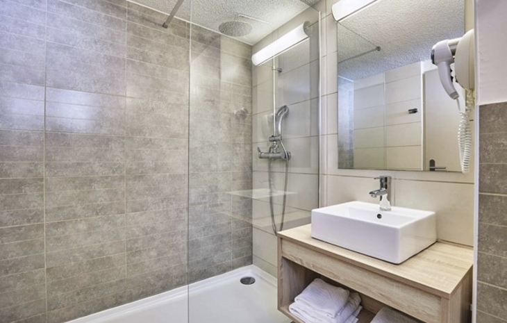 Modernes Badezimmer mit Dusche, Waschtisch, Handtüchern und Haartrockner