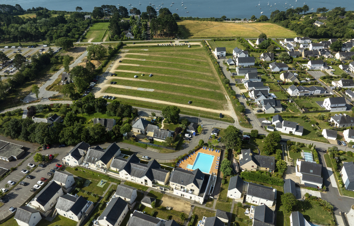 Luftaufnahme einer Ferienanlage mit Swimmingpool, umgeben von Häusern und grünen Feldern.