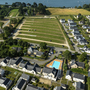 Luftaufnahme einer Ferienanlage mit Swimmingpool, umgeben von Häusern und grünen Feldern.