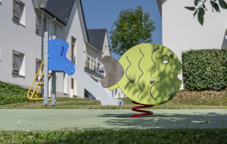 Spielplatz mit Wippgerät in Fischform vor Ferienanlage