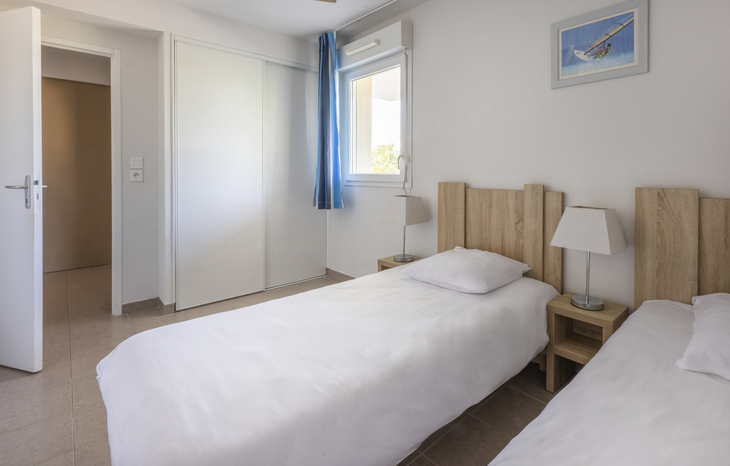 Helles Schlafzimmer mit zwei Einzelbetten, Nachttischlampen und einem Fenster.