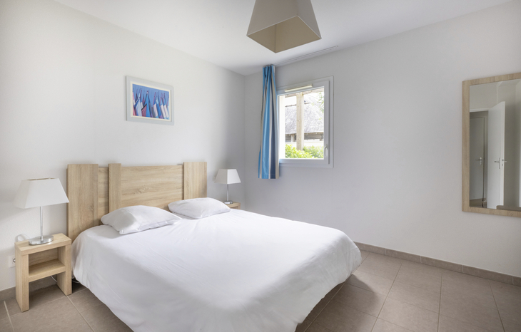 Modernes Schlafzimmer mit Doppelbett, weißen Wänden und blauem Vorhang.