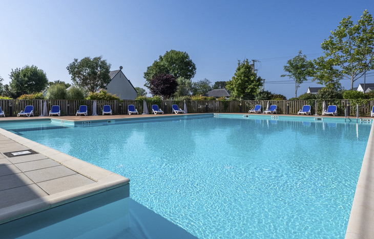 Poolbereich mit Liegestühlen in einer Ferienanlage bei sonnigem Wetter.