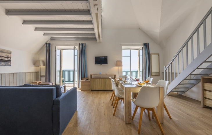 Helles Wohnzimmer mit Esstisch, Treppe und offenem Zugang zum Balkon.
