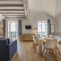 Helles Wohnzimmer mit Esstisch, Treppe und offenem Zugang zum Balkon.