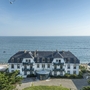 Weiße Residenz am Meer mit blauen Balkonen, umgeben von Bäumen, im Hintergrund der Ozean.