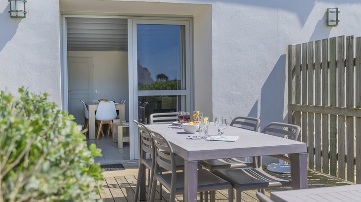Terrasse mit Esstisch und Stühlen vor einem Ferienhaus.