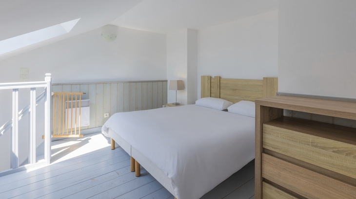Helles Schlafzimmer mit Doppelbett, Holzkommode und Gitterbett in moderner Einrichtung.