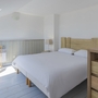 Helles Schlafzimmer mit Doppelbett, Holzkommode und Gitterbett in moderner Einrichtung.