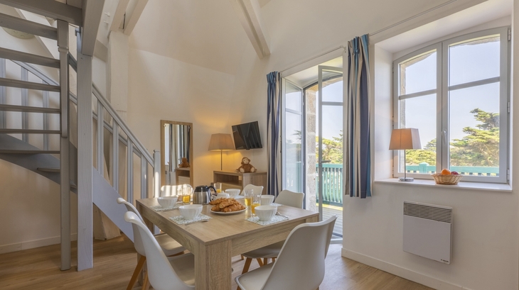 Essbereich in heller Ferienwohnung mit Holztisch und Treppe.
