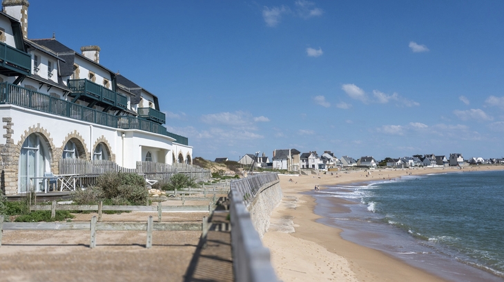 Küstenlandschaft mit Gebäuden am Strand und blauem Himmel.