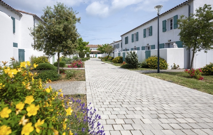Gepflegter Gartenweg zwischen weißen Gebäuden mit grünen Fensterläden