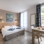 Helles Hotelzimmer mit Doppelbett, Schreibtisch und Fenster mit Vorhängen.