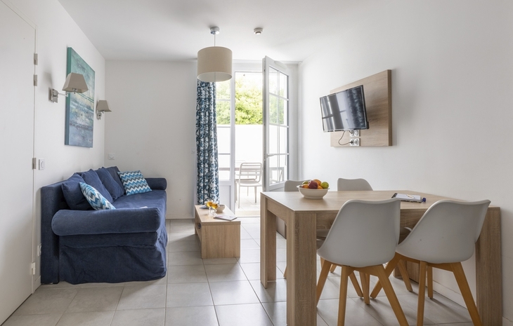 Helles Wohnzimmer mit Sofa, Esstisch, Stühlen und TV, Blick auf Terrasse.