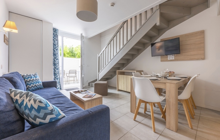 Wohnbereich mit Sofa, Esstisch und Treppe in modernem Ferienapartment.