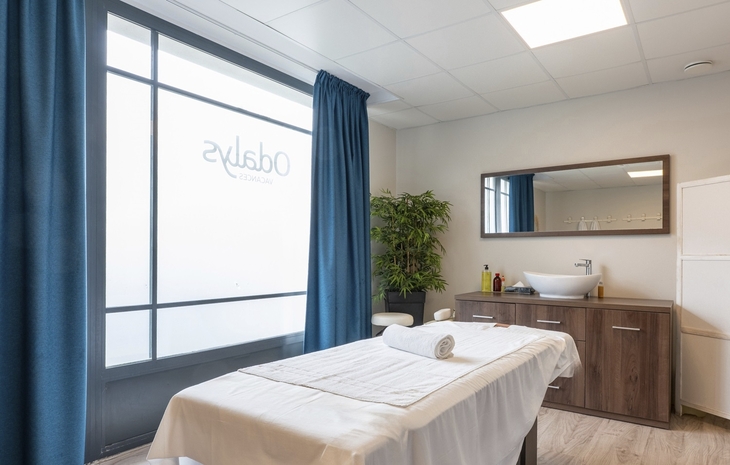 Massageraum mit Massagebett bei Odalys, blauer Vorhang, Waschbecken und Spiegel.