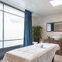 Massageraum mit Massagebett bei Odalys, blauer Vorhang, Waschbecken und Spiegel.
