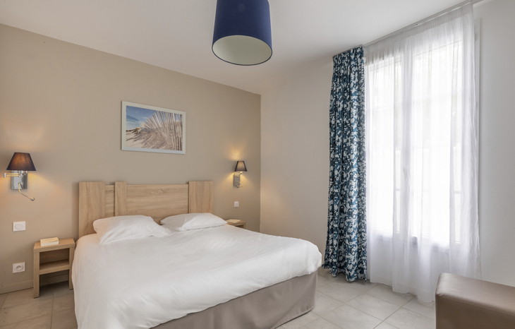 Helles Schlafzimmer mit Doppelbett und blauer Vorhang vor großem Fenster.
