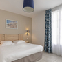 Helles Schlafzimmer mit Doppelbett und blauer Vorhang vor großem Fenster.