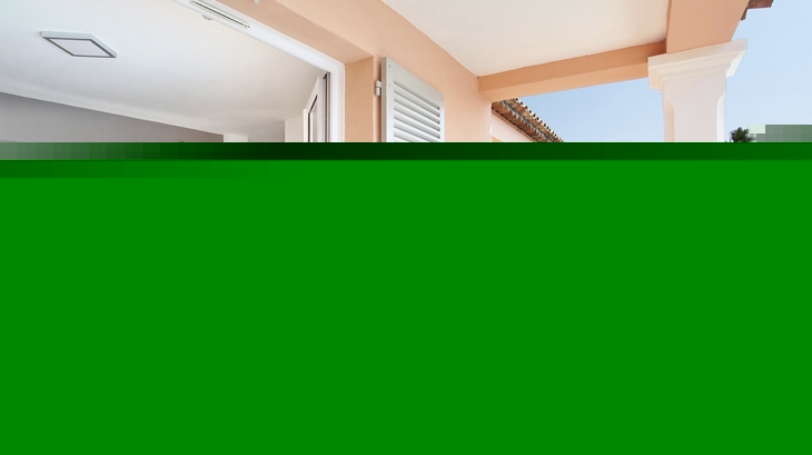 Balkon mit Tisch, Frühstücksset und Blick auf grüne Umgebung und Gebäude.