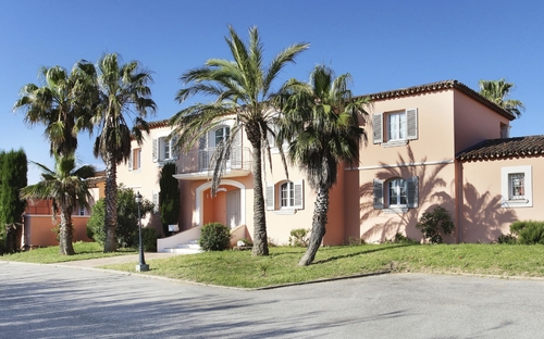 Haus im mediterranen Stil mit Palmen und Garten im Vordergrund.