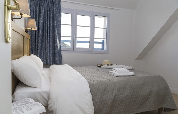 Doppelzimmer in der Résidence mit Bett, Fenster und blauen Vorhängen.