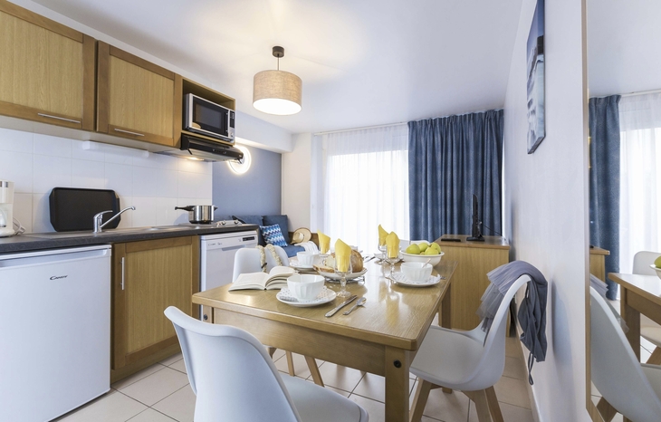 Essbereich mit Holztisch, weißen Stühlen und Küchenzeile in heller Ferienwohnung.
