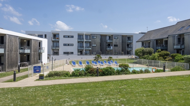 Wohnanlage mit Pool und Liegestühlen im Freien vor modernen Gebäuden.