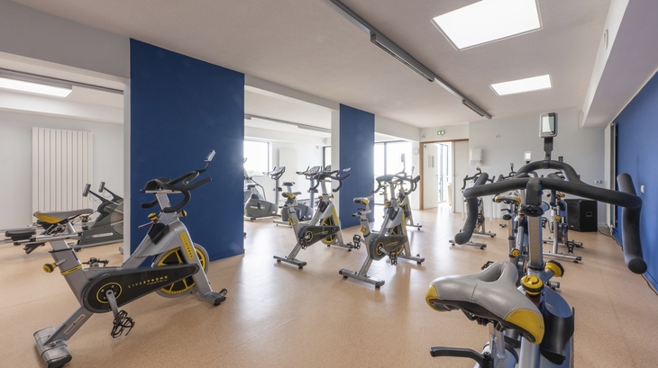 Fitnessraum mit mehreren stationären Fahrrädern und blauem Trennwandsystem.