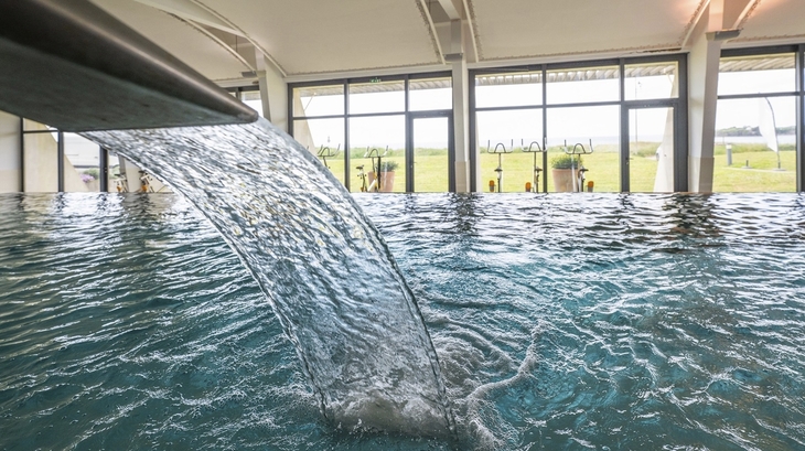 Innenpool mit Wasserfall und großen Fenstern im Hintergrund.