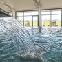 Innenpool mit Wasserfall und großen Fenstern im Hintergrund.