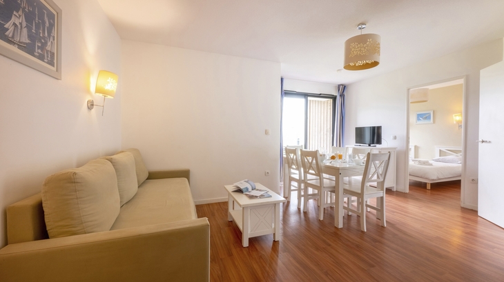 Wohnraum in Ferienwohnung mit Sofa, Esstisch und TV auf Holzboden.
