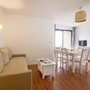 Wohnraum in Ferienwohnung mit Sofa, Esstisch und TV auf Holzboden.
